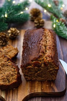 a loaf of banana bread on a cutting board with pine cones and lights in the background