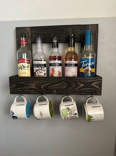 a wooden shelf holding four cups and two mugs on top of each other with different types of alcohol in them