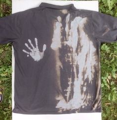 a tie - dye shirt with a hand print on it sitting in the grass next to a pair of shoes