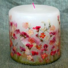 a white candle with pink and red flowers on it sitting on a gray cloth covered surface