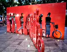 a group of people standing next to each other near a red wall with bikes on it