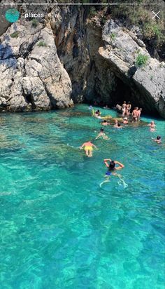 people swimming in clear blue water next to large rocks