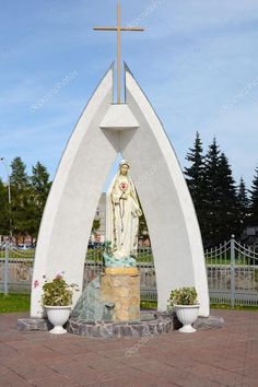 a statue of the virgin mary in front of a white arch with a cross on top