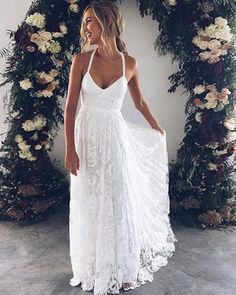 a woman standing in front of a floral arch wearing a white dress with spaghetti straps