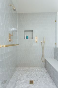 a white tiled bathroom with gold fixtures and shower head, along with marble flooring