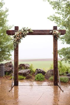 a wooden arch with flowers and greenery on it for an outdoor wedding ceremony in the rain