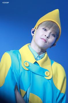 a boy in a yellow and blue outfit with his hands on his hips, looking at the camera