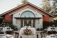 an outdoor dining area with tables and chairs set up for a formal dinner in front of a brick building