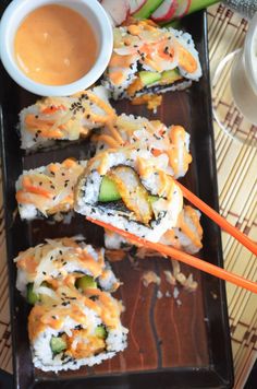 some sushi rolls are on a tray with chopsticks and dipping sauce in the background