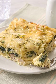 a white plate topped with lasagna covered in cheese and spinach next to a glass of milk