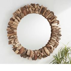 a circular mirror made out of driftwood sitting on top of a wall next to a potted plant