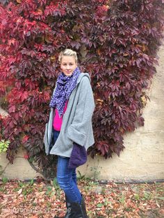 a woman standing in front of a bush with red leaves on it and wearing a scarf around her neck