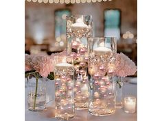 a table topped with lots of vases filled with flowers and lite up candles