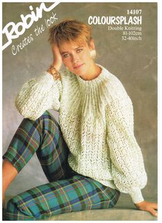 a woman wearing plaid pants and a white sweater is sitting on the ground with her hand in her hair