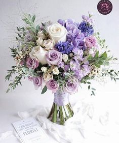 a vase filled with purple and white flowers sitting on top of a table next to a book