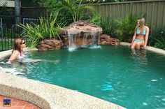 two women are sitting in the pool with waterfall