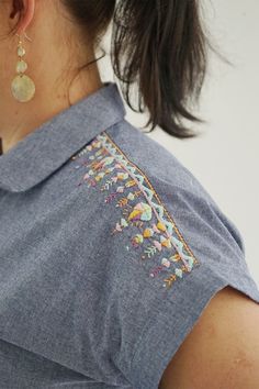 a woman wearing a blue shirt with embroidered designs on it