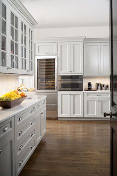 a large kitchen with white cabinets and wood flooring, along with a bowl of fruit on the counter