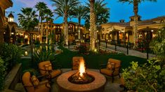 an outdoor fire pit surrounded by palm trees and lawn chairs with lights on the top