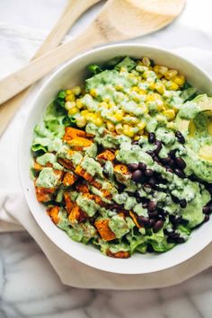 a bowl filled with black beans, corn and guacamole next to a wooden spoon