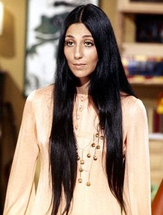 a woman with long black hair standing in front of a book shelf