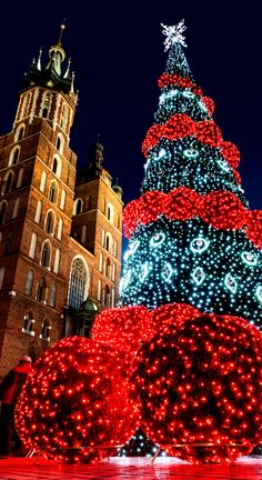 a large christmas tree is lit up in front of an old building with a clock tower