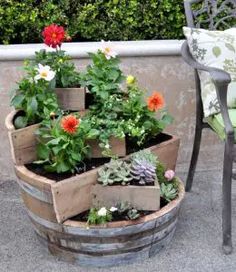 an outdoor garden with flowers and plants in wooden containers on the ground next to a chair