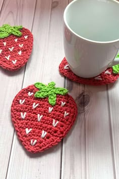 two crocheted strawberry coasters sitting next to a cup