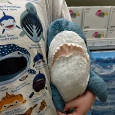 a person holding a stuffed shark in their arms with other items on it's back