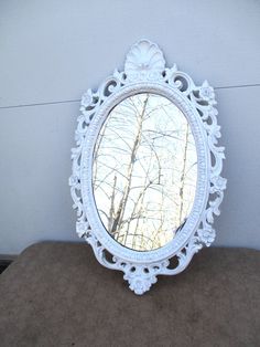 a white mirror sitting on top of a wooden table next to a wall with trees in the background