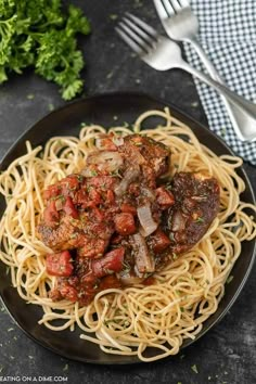 pasta with meat and tomato sauce on a black plate next to a fork, knife and parsley