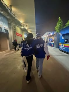 two people are walking down the street at night, one is wearing a blue and white jacket