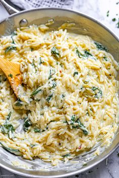 pasta with spinach and cheese in a skillet on a marble counter top next to a wooden spoon