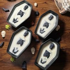 three black trays filled with white frosting and skulls on top of a wooden table