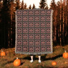 a woman standing in front of a blanket with pumpkins on it and trees behind her