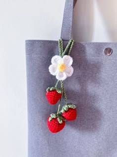 a crocheted flower and two strawberries hanging from a gray tote bag