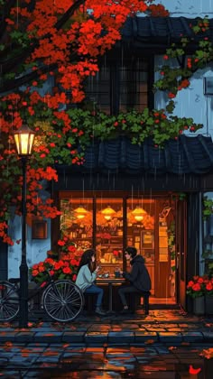 two people sitting at a table in front of a store with autumn leaves on the tree