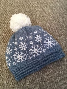 a blue and white knitted beanie with snowflakes on the top, sitting on carpet