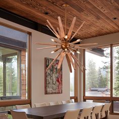 a dining room table with chairs and a chandelier hanging from the ceiling in front of large windows