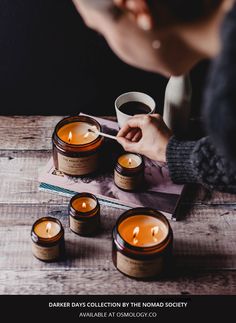 a person lighting candles on top of a wooden table next to books and a cup