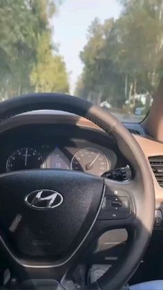 the steering wheel and dashboard of a car on a road with trees in the background