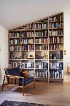 a living room filled with lots of books on top of a wooden shelf next to a chair