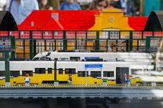 a lego model of a yellow and white train on tracks with people standing near by