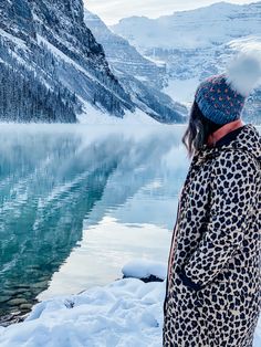 a woman standing on top of a snow covered slope next to a lake