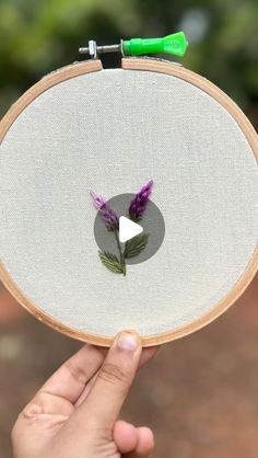 someone is holding up a embroidery project with purple flowers on the front and white back