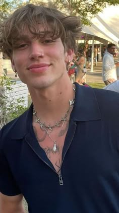 a young man wearing a blue shirt and silver necklace with his hair blowing in the wind