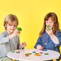 two children playing with buttons on a white table in front of a bright yellow background