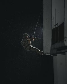 a man in the air while holding onto a rope on a building at night time