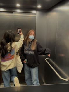 two girls wearing face masks while standing on an escalator with their hands in the air