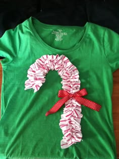 a green t - shirt with red and white ruffles on it, sitting on top of a wooden floor